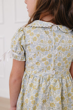 A young girl models a vintage-inspired floral dress featuring a classic Peter Pan collar, short puff sleeves, and a buttoned back.