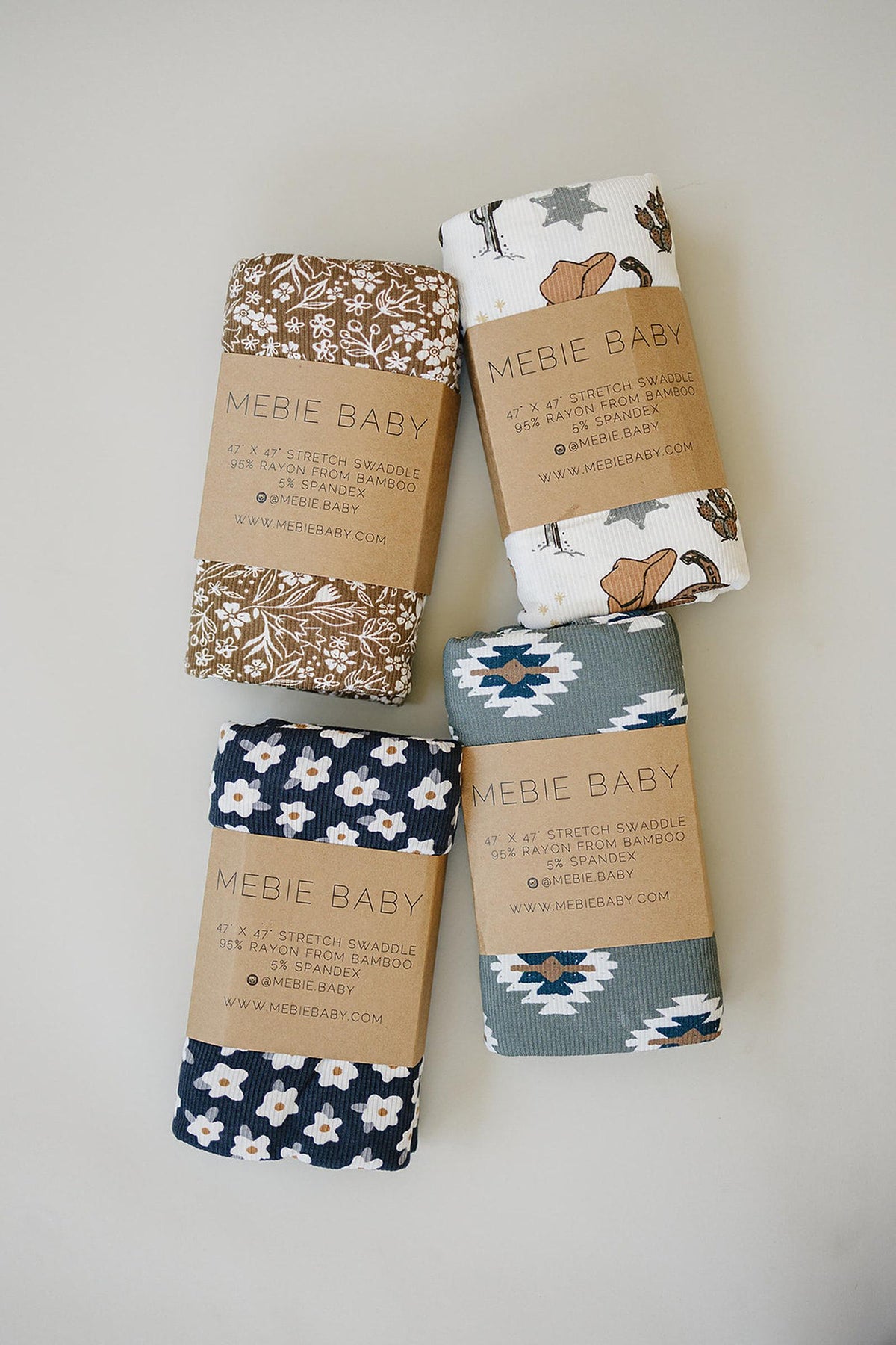 Four rolled swaddles from Mebie Baby, featuring patterns in navy, brown, and gray, showcasing soft bamboo fabric.