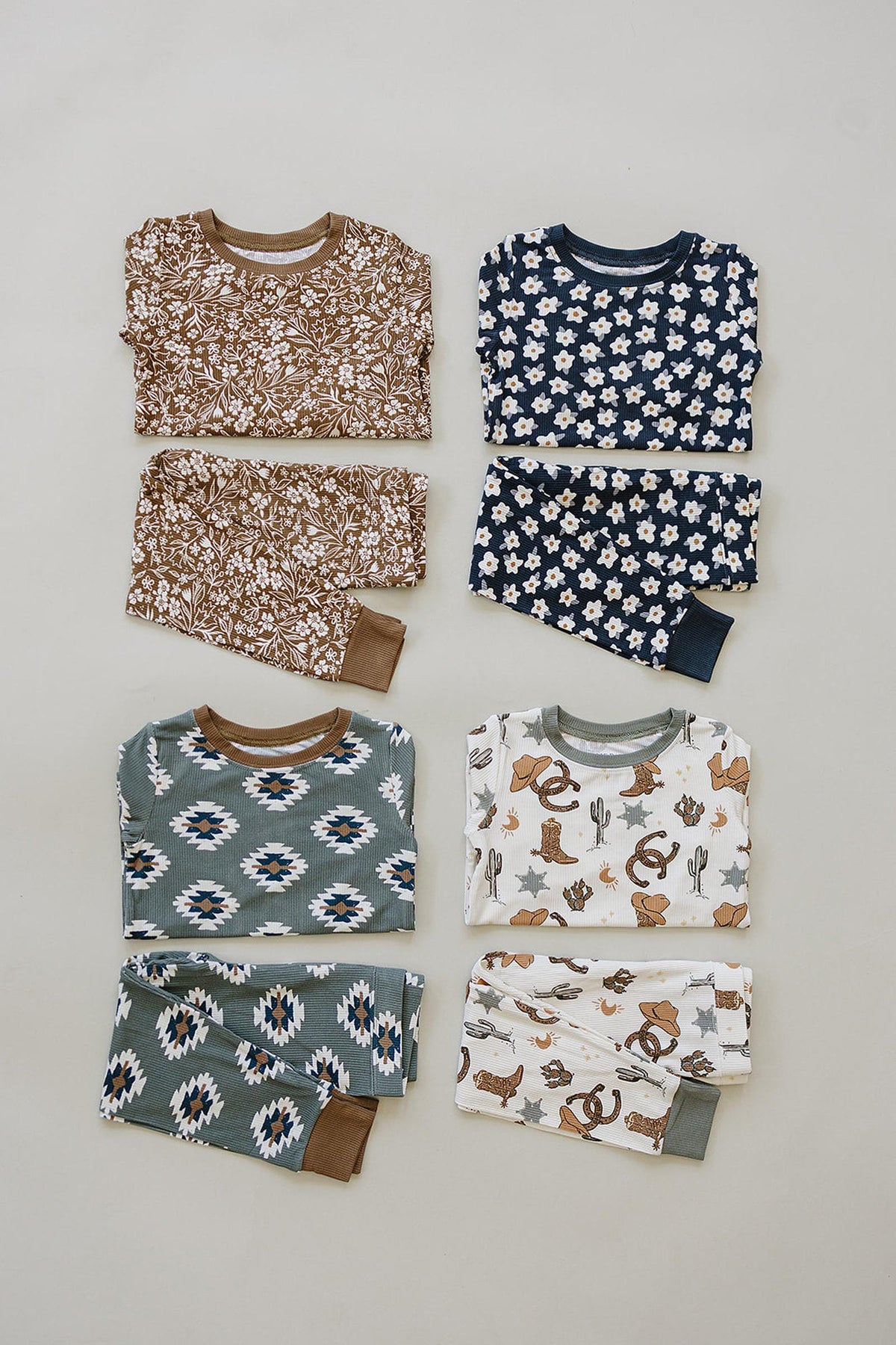 Four folded pajama sets with floral, geometric, and western patterns in brown, navy, and green color schemes.