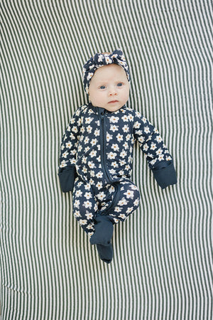 A baby in navy daisy-patterned pajamas and matching headband lies on a striped background.