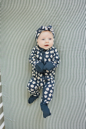 A baby in navy daisy-patterned pajamas with matching headband lies on a striped green and white blanket.
