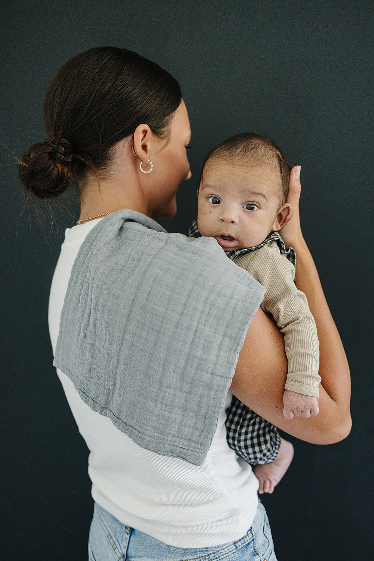 A woman holds a baby over her shoulder, using a dusty blue muslin burp cloth.