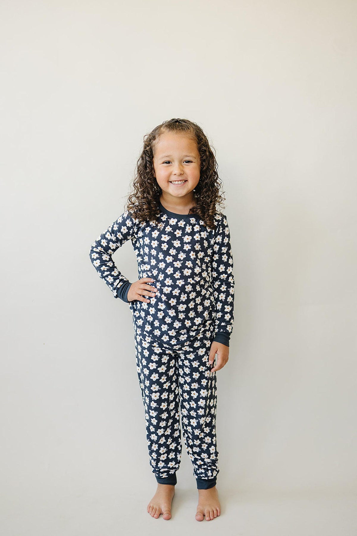 A child wearing a navy pajama set with white daisy patterns stands smiling against a plain background.