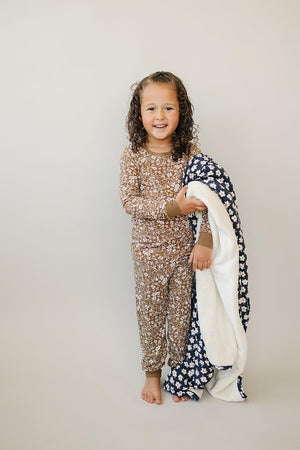 Child in brown floral pajama set holding a navy floral blanket, standing against a plain background.