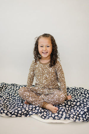 A child in a brown floral pajama set sits on a blue floral blanket, smiling at the camera.