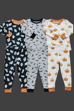 Four sets of Halloween-themed pajamas featuring ghost, bat, and pumpkin prints, in various colors with orange cuffs.