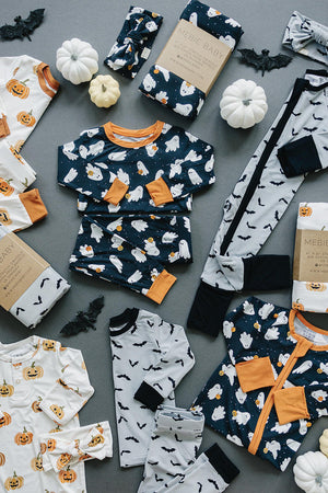 Halloween-themed childrens pajamas with ghost and pumpkin prints displayed on a gray surface, featuring bamboo fabric.