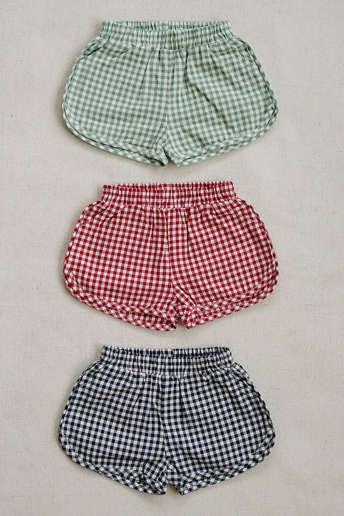 Three gingham shorts in green, red, and navy are displayed on a neutral background, showcasing different color options.