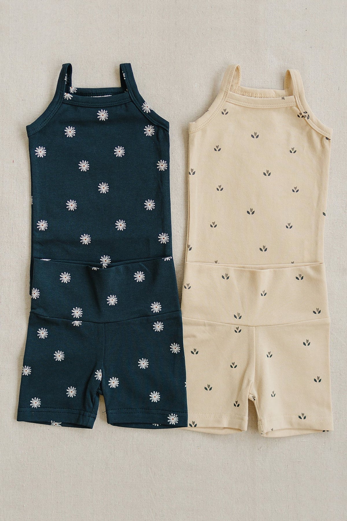 Two baby tank top and biker shorts sets: navy with daisy print, beige with small floral pattern.
