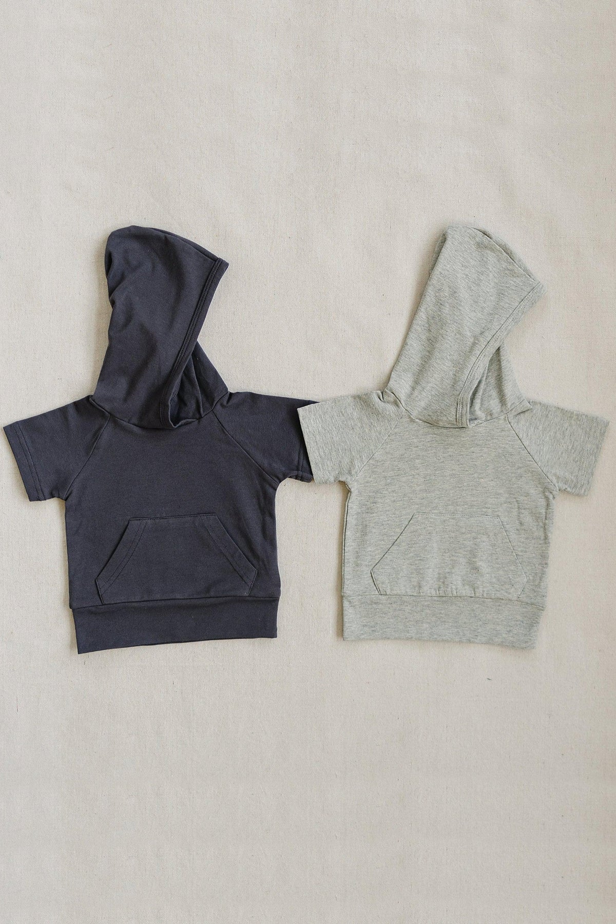 Two short-sleeve hooded t-shirts are displayed, one in dark grey and the other in light heather grey, featuring front pockets.