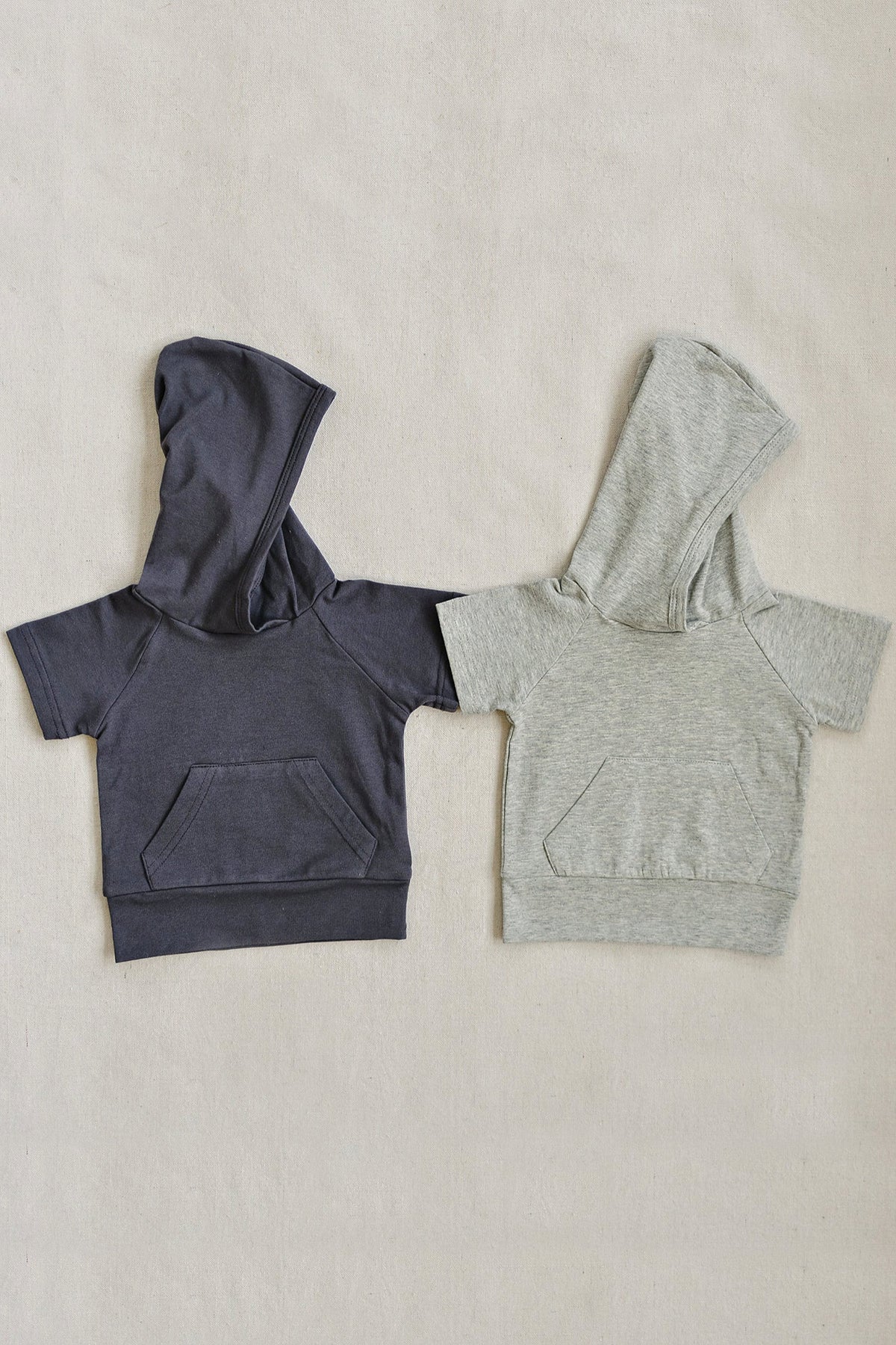 Two hooded t-shirts for toddlers, one in slate gray and the other in light gray, on a neutral background.