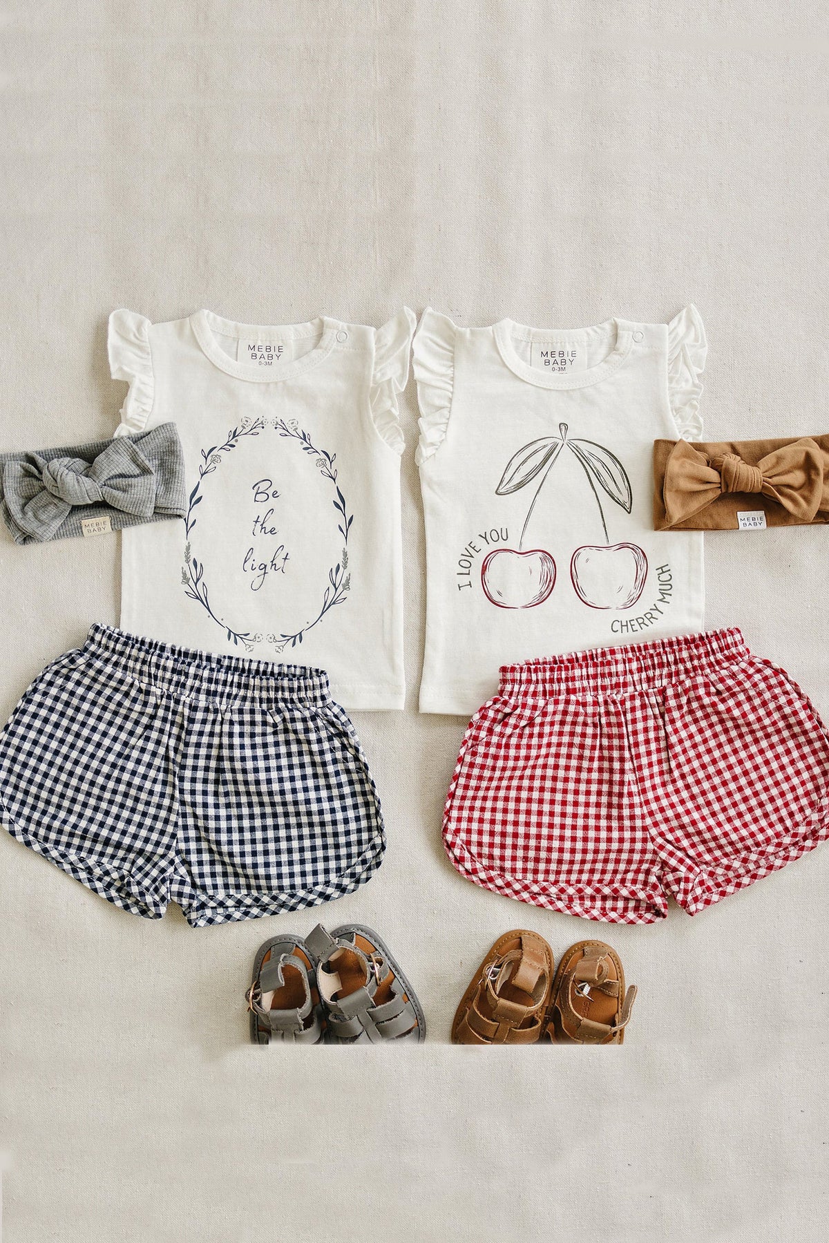 Two Mebie Baby ruffle T-shirts with cherry and floral designs, paired with gingham shorts and bow headbands.