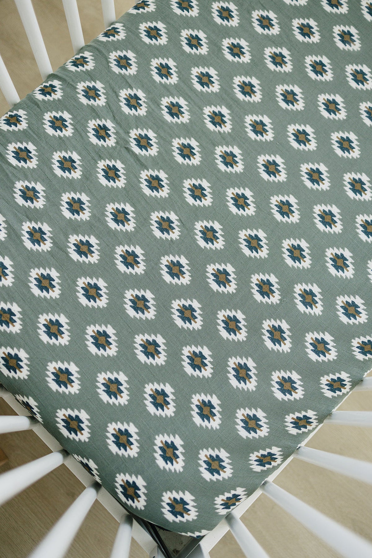 Green crib sheet with a white and brown Aztec pattern, made of soft muslin fabric, fitted on a crib.