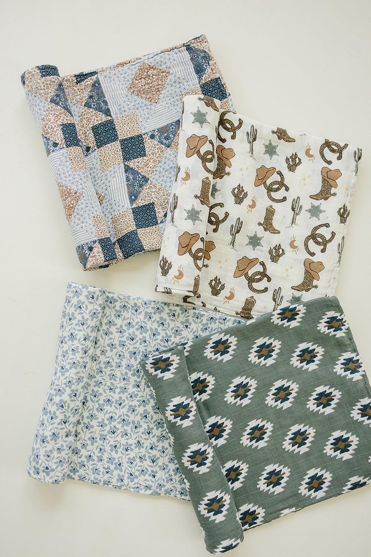 Four cotton swaddle blankets with diverse patterns, including patchwork, cowboy-themed, floral, and geometric Aztec designs, are displayed.