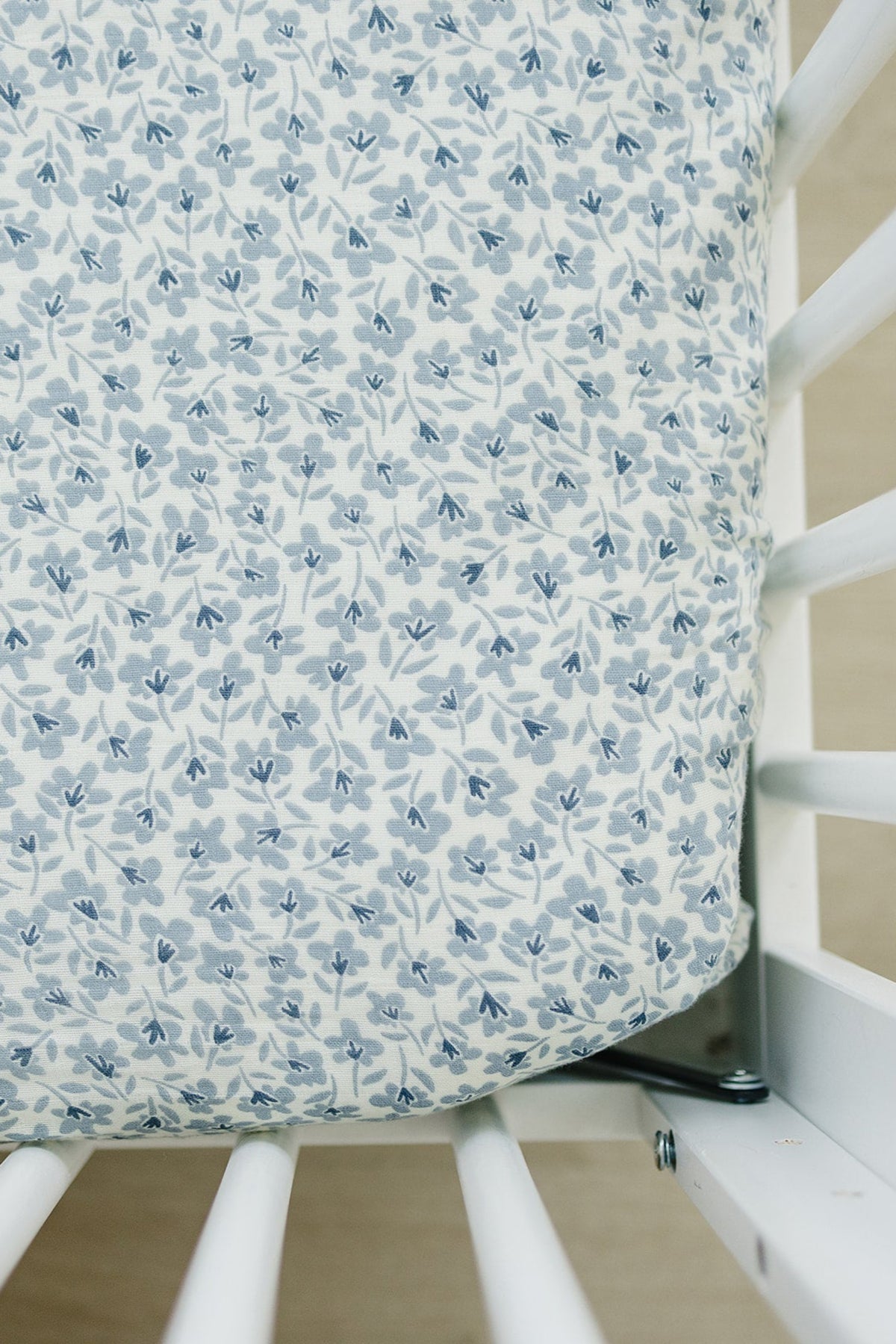 Blue floral muslin crib sheet on white crib, showcasing delicate leaf and flower pattern. Made from 100% cotton.