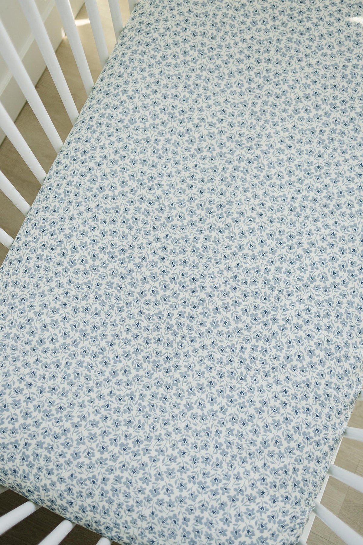 Blue floral muslin crib sheet on a white crib, featuring a delicate, intricate pattern for a cozy nursery.