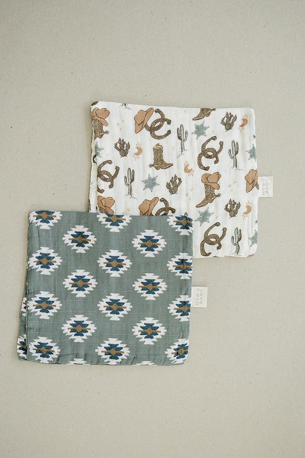 Two muslin burp cloths, one with a Southwest Aztec pattern and the other with cowboy-themed prints, on beige background.