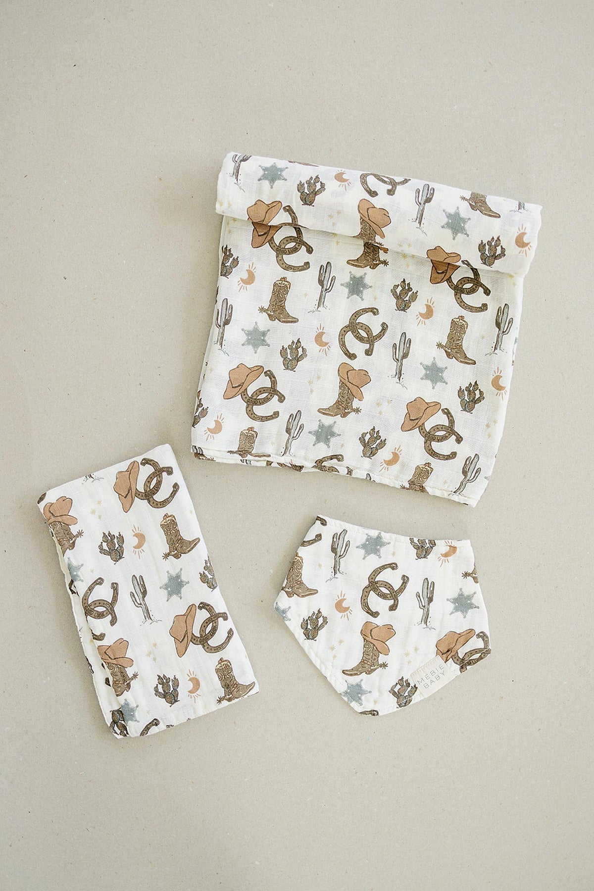 Three pieces of muslin fabric with cowboy-themed prints, featuring hats, boots, and cacti on a neutral background.