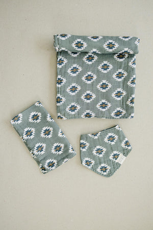 Three pieces of green fabric with a Southwest Aztec pattern, including a bib, folded cloth, and blanket.