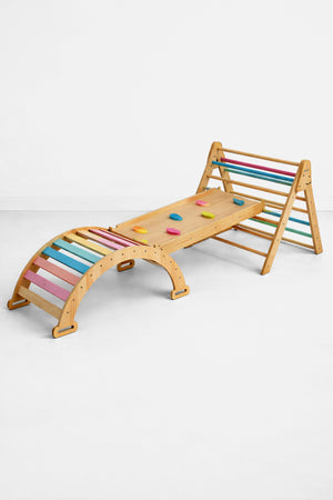 A wooden Pikler triangle playset featuring a slide and rocker, adorned with pastel-colored climbing grips. The sustainable design encourages active play for toddlers and enhances imaginative exploration.