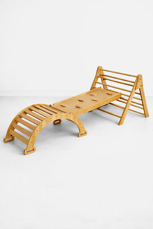 A wooden Pikler triangle playset in a natural finish features a climbing structure and slide. It is designed for toddlers, promoting active play and imaginative exploration in a safe environment.