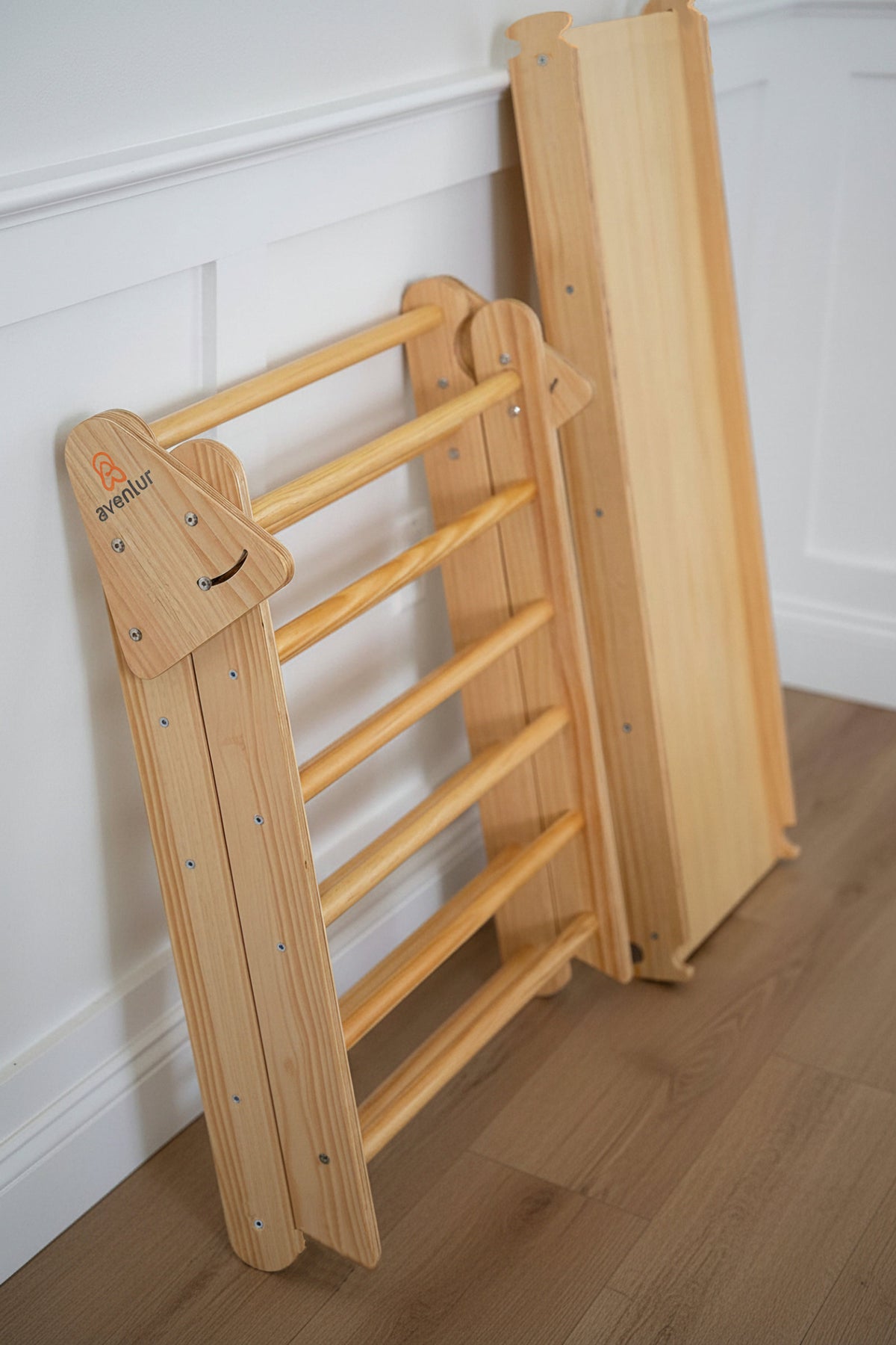 A natural wooden Pikler triangle playset is shown in a bright indoor setting. The foldable design features smooth, rounded edges, highlighting its sustainable construction and child-friendly features.