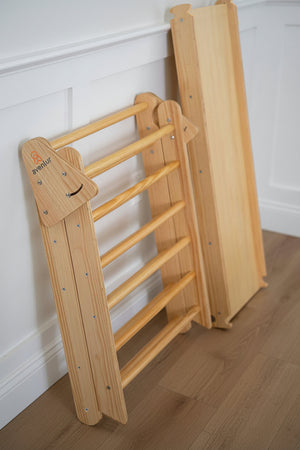 A natural wooden Pikler triangle playset is shown in a bright indoor setting. The foldable design features smooth, rounded edges, highlighting its sustainable construction and child-friendly features.