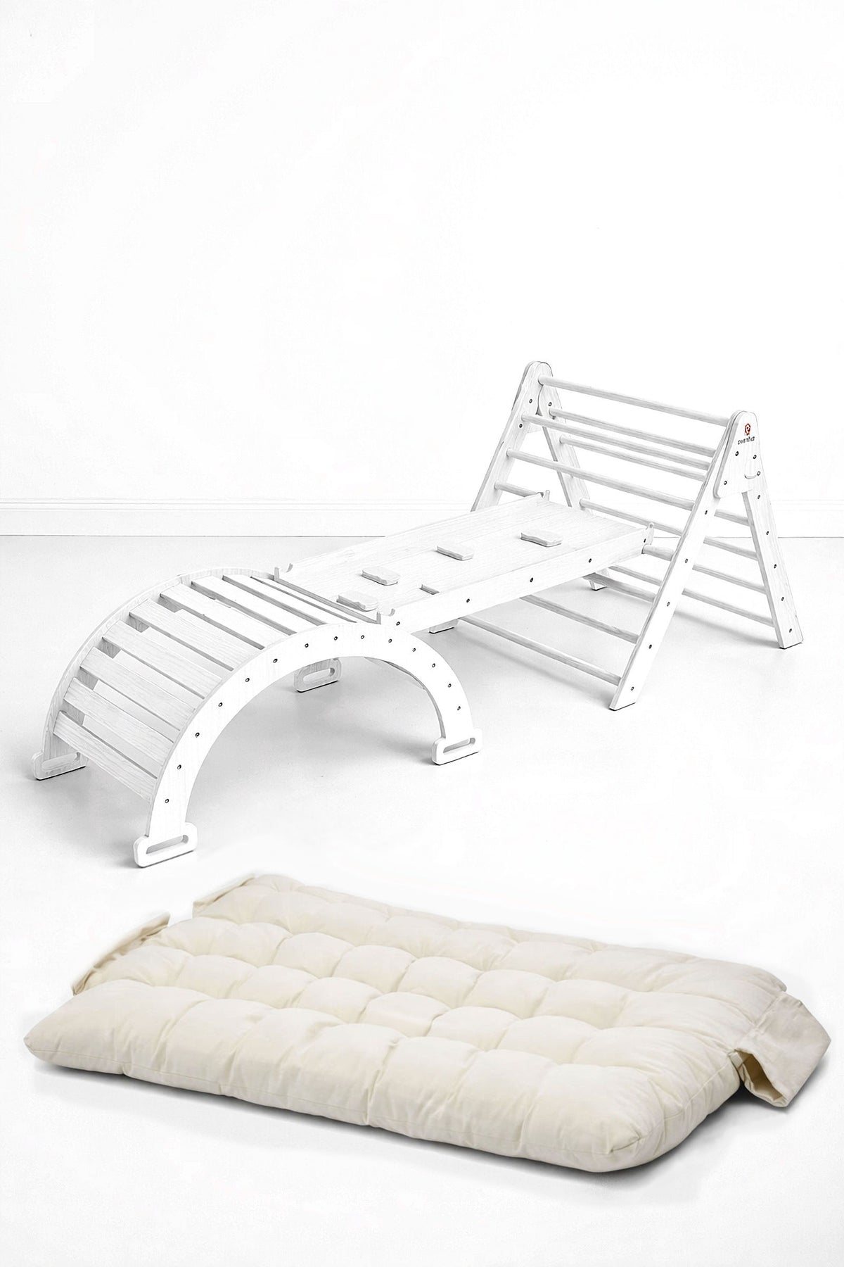 The image features a white wooden Pikler triangle playset alongside a thick, cream-colored cushion. This eco-friendly, modular design promotes active play and comfort for toddlers and young children.