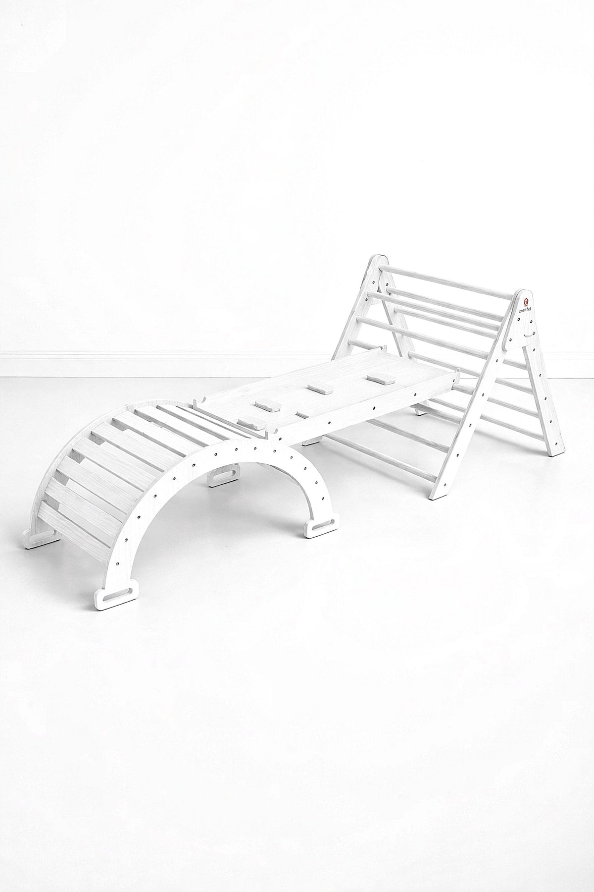A white wooden climbing playset features a Pikler triangle and slide, designed for indoor active play. Its sturdy construction is suitable for toddlers, promoting movement and imaginative exploration.