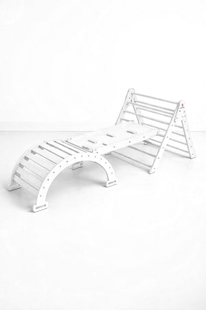 A white wooden climbing playset features a Pikler triangle and slide, designed for indoor active play. Its sturdy construction is suitable for toddlers, promoting movement and imaginative exploration.