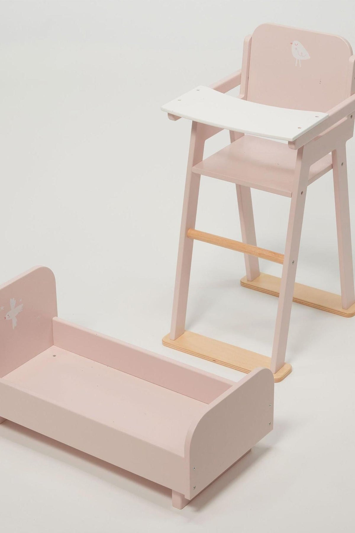 Pink wooden baby doll high chair and crib with white accents, featuring bird designs, on a light background.