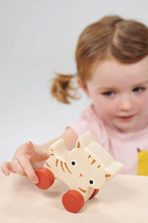 Child playing with a wooden toy cat on a light surface.