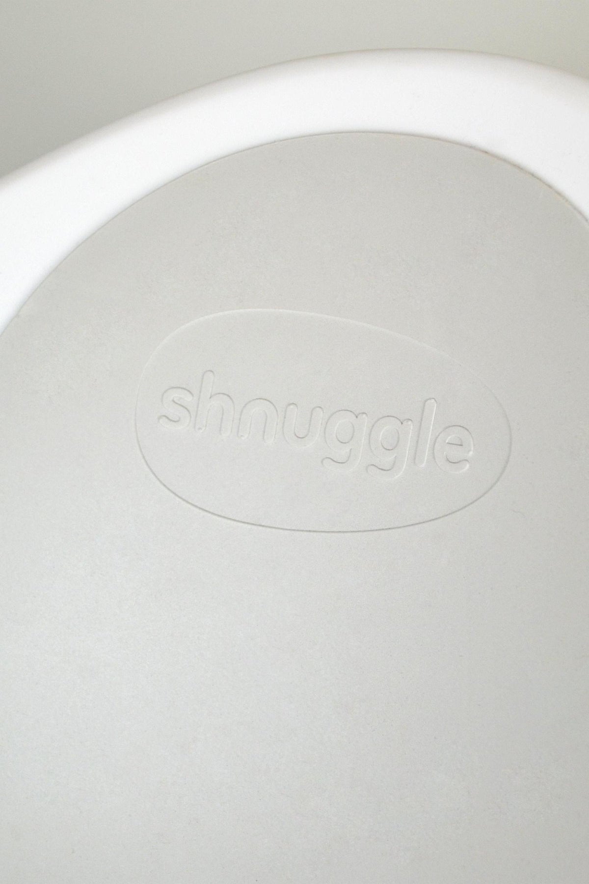 Close-up of the Shnuggle logo embossed on a light beige surface, showcasing a minimalist design.