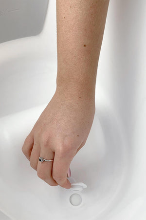 A hand with a ring holds a white plug over a drain in a white basin.