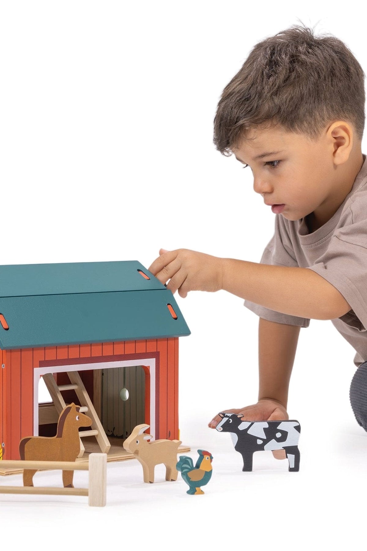 Child playing with a toy barn set on a white background