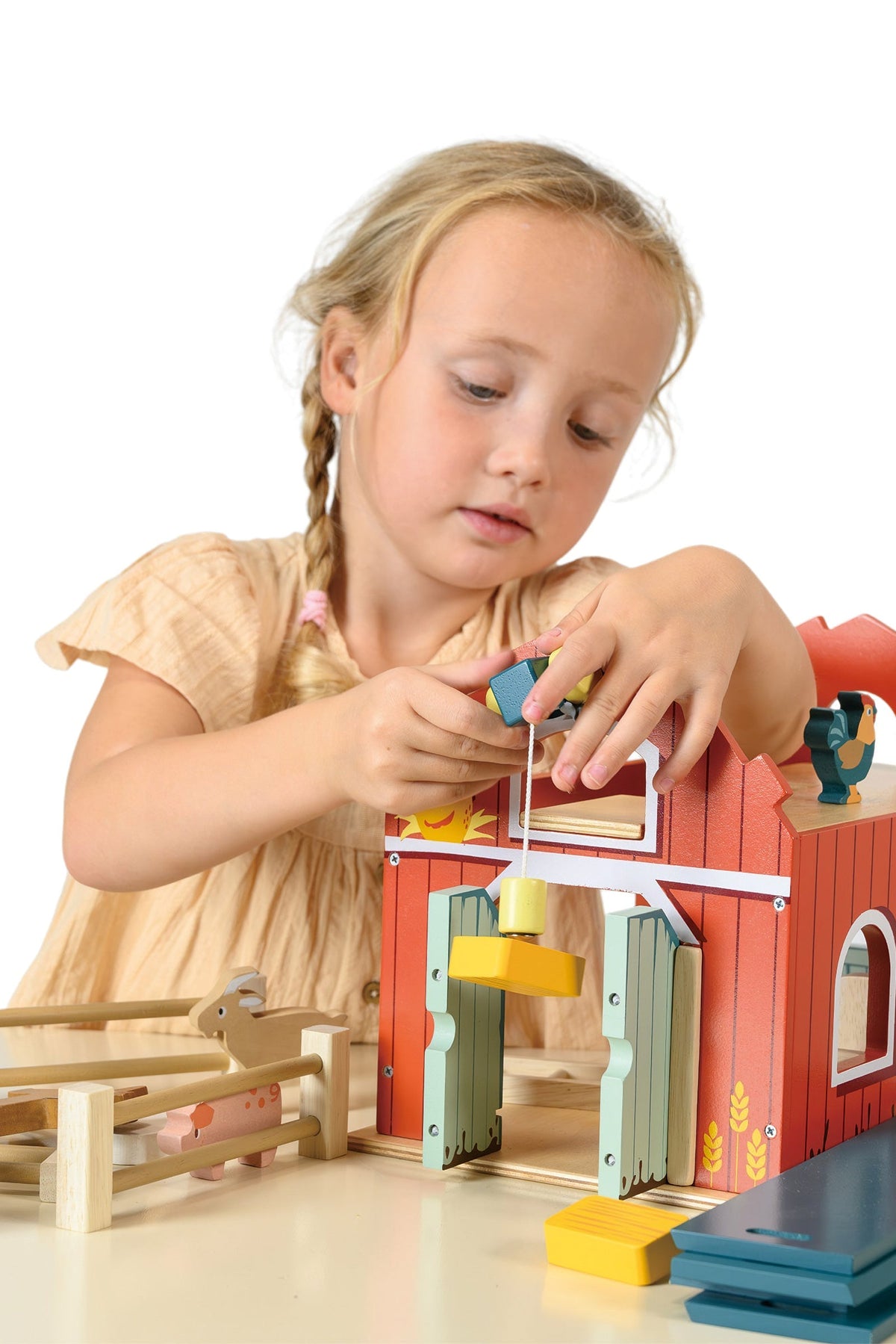 Child playing with a colorful toy wooden barn on a white background