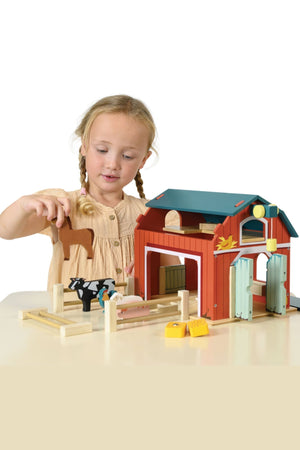 Child playing with a wooden toy barn set on a white background