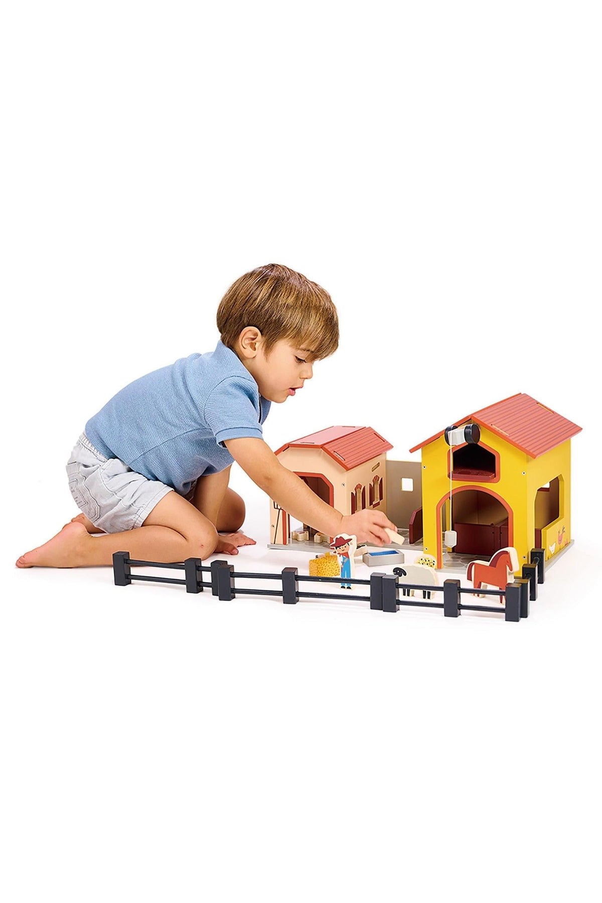 A child plays with a colorful wooden farm playset, featuring a barn, stable, and animal figures.
