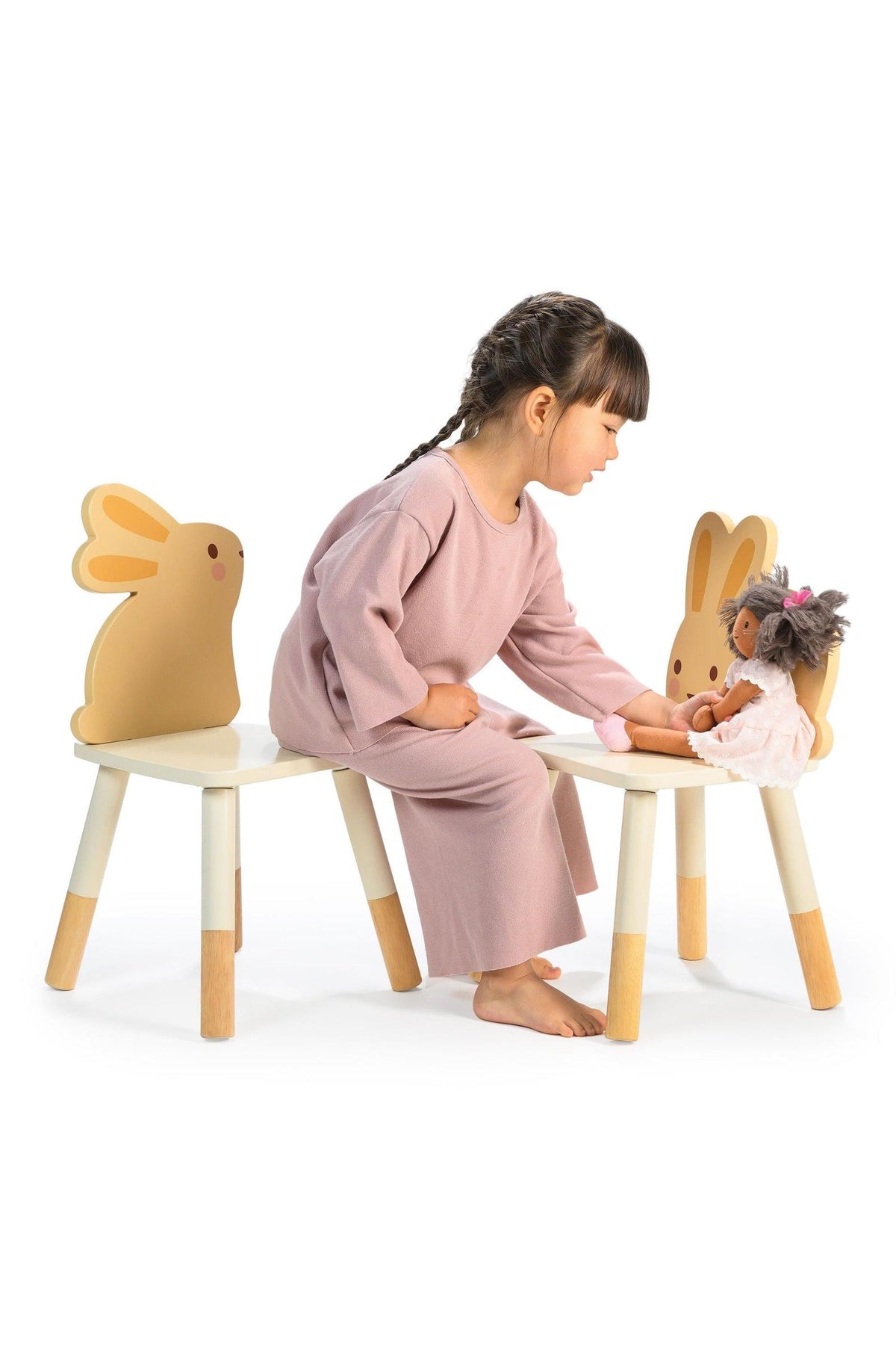 A child in a pink outfit plays with a doll on a bunny-themed chair set with wooden legs.
