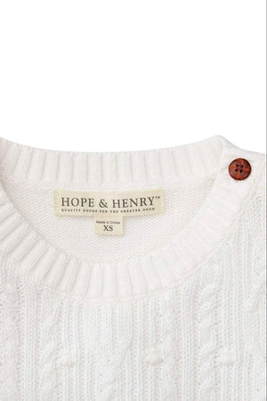 Close-up of a soft white cable knit sweater featuring a round neckline, a brown button, and a Hope & Henry.