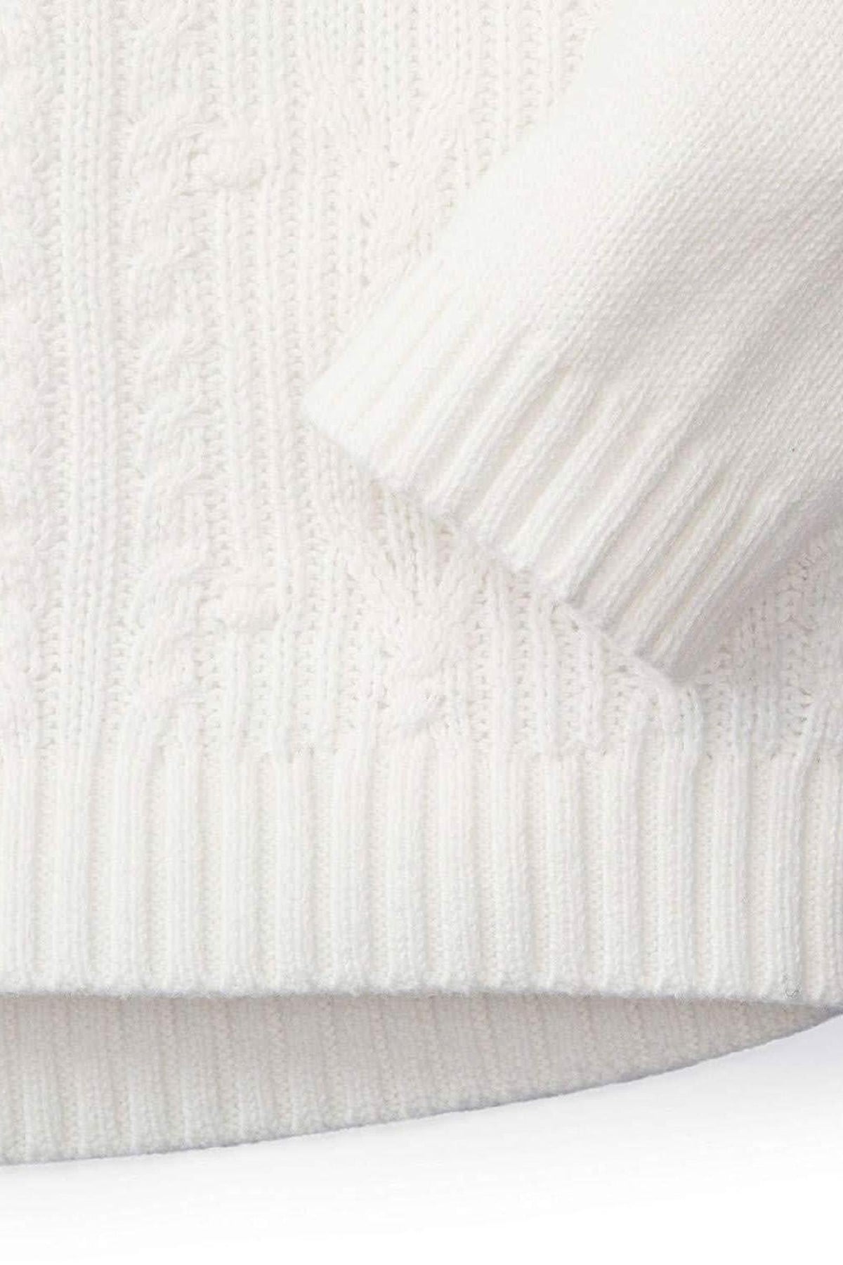Close-up of a soft white organic cotton cable knit sweater with ribbed cuffs, showcasing its cozy texture and design.