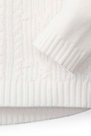 Close-up of a soft white organic cotton cable knit sweater with ribbed cuffs, showcasing its cozy texture and design.