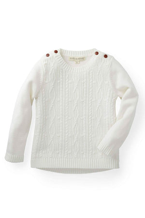 White cable knit sweater for girls by Hope & Henry, featuring faux leather shoulder buttons and soft, organic cotton material.