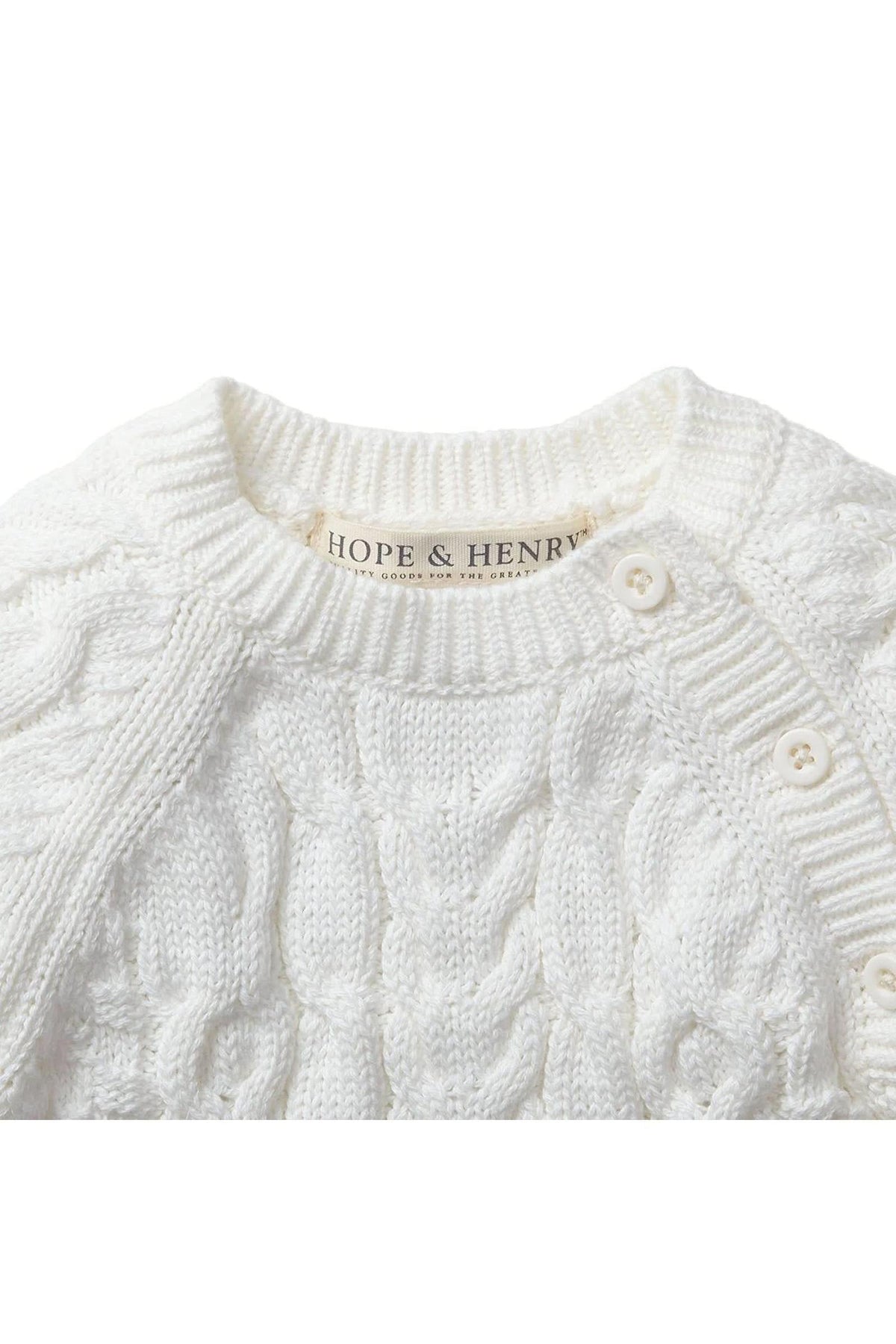 Close-up of a soft white cable knit sweater romper by Hope & Henry, featuring button openings at the shoulder. Made from 100% organic cotton, its designed for babies comfort.