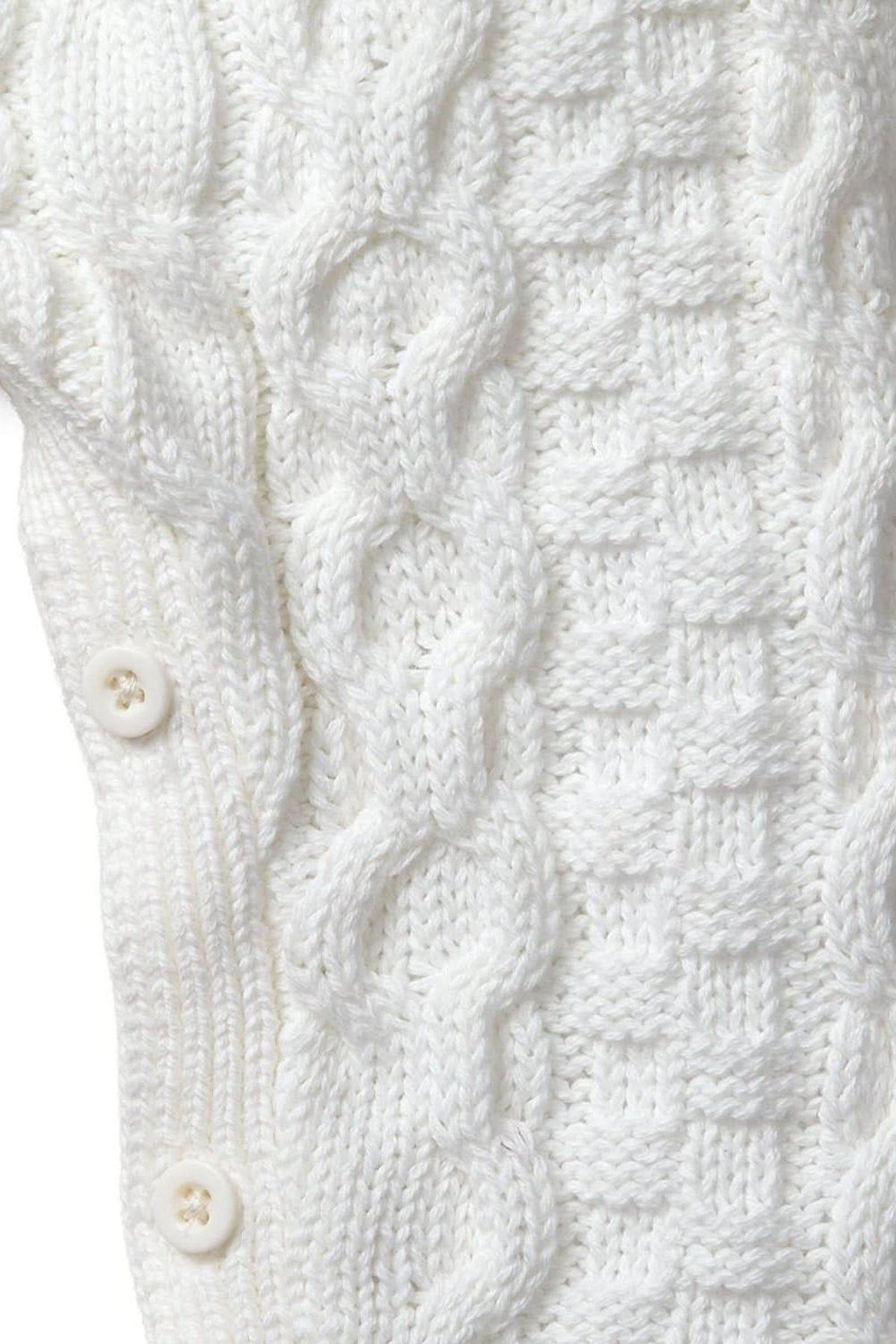 Close-up of a soft white cable knit sweater romper featuring intricate patterns and button closures. Made from 100% organic cotton, it offers a cozy, heirloom-quality piece for babies.