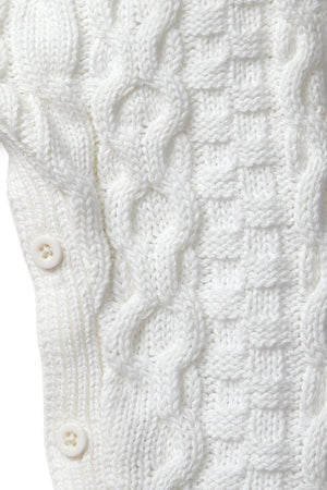 Close-up of a soft white cable knit sweater romper featuring intricate patterns and button closures. Made from 100% organic cotton, it offers a cozy, heirloom-quality piece for babies.