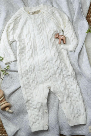 A soft white cable knit romper by Hope & Henry is laid out on a light gray blanket, featuring button openings for easy dressing.