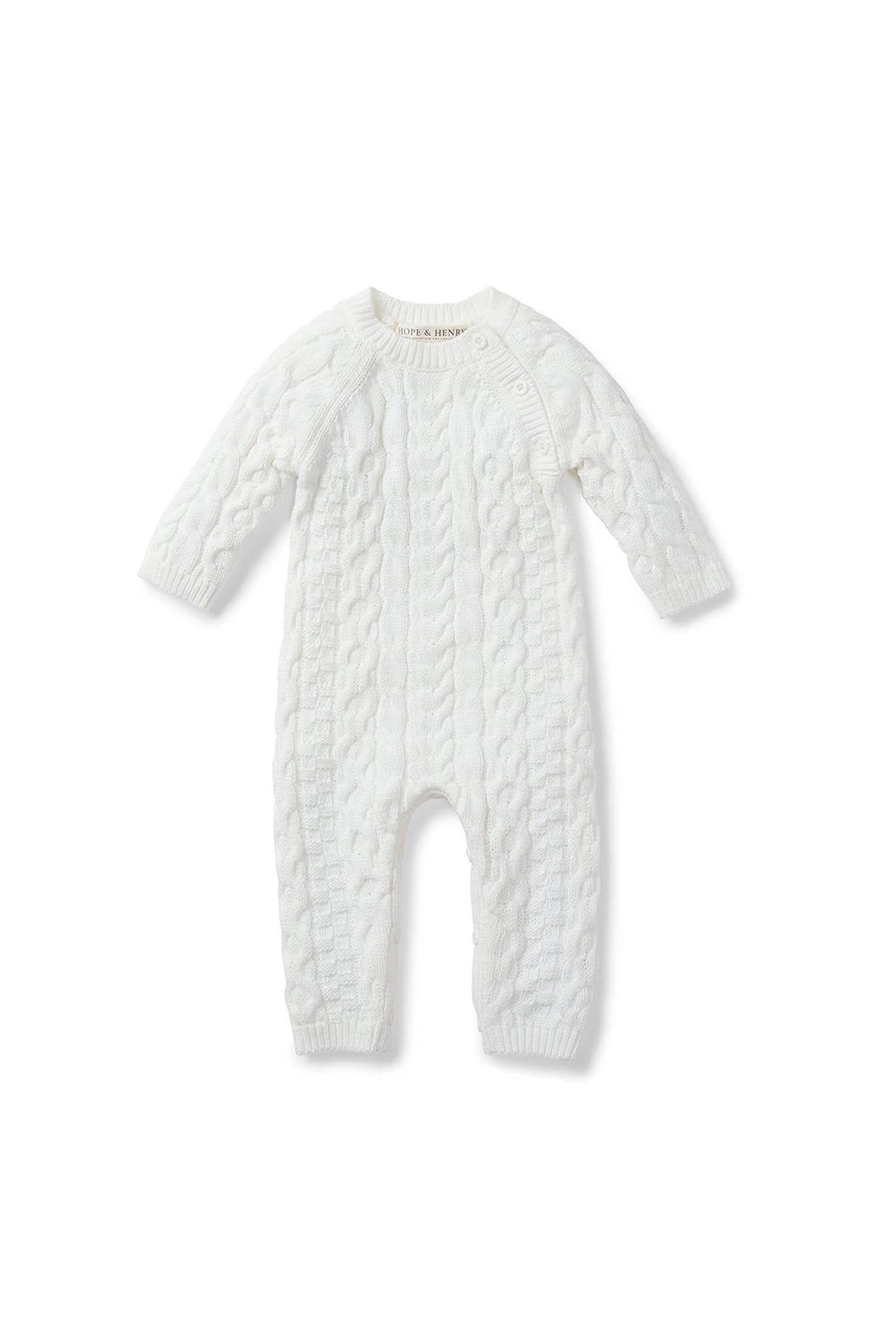 A soft white cable knit romper for babies features long sleeves and button openings at the shoulder. Made from 100% organic cotton, it combines comfort with eco-friendly design.