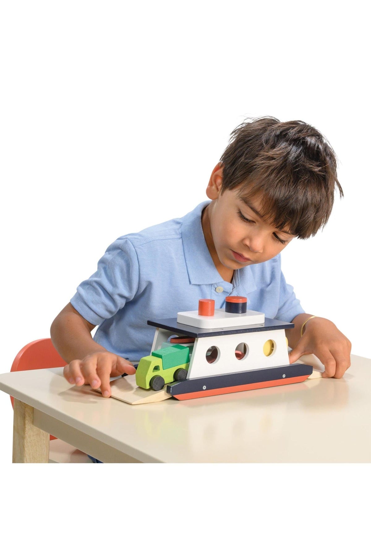 A child in a blue shirt plays with a colorful wooden car ferry toy on a table.