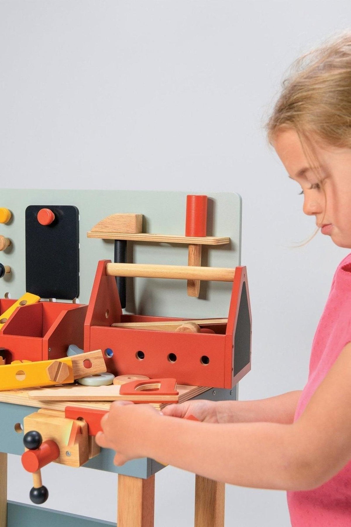 A child plays with a colorful wooden carpenters workshop, featuring tools and a workbench, promoting imaginative play.